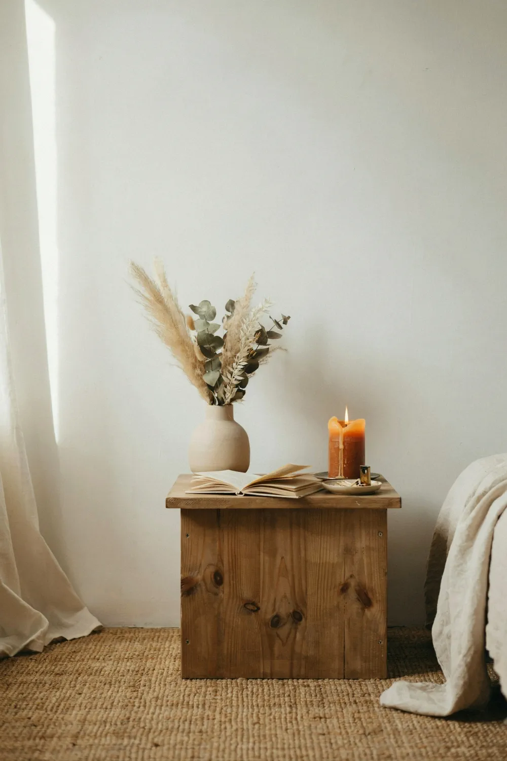 Earthy bedroom nightstand styled with a lit candle, dried botanicals, and a jute rug