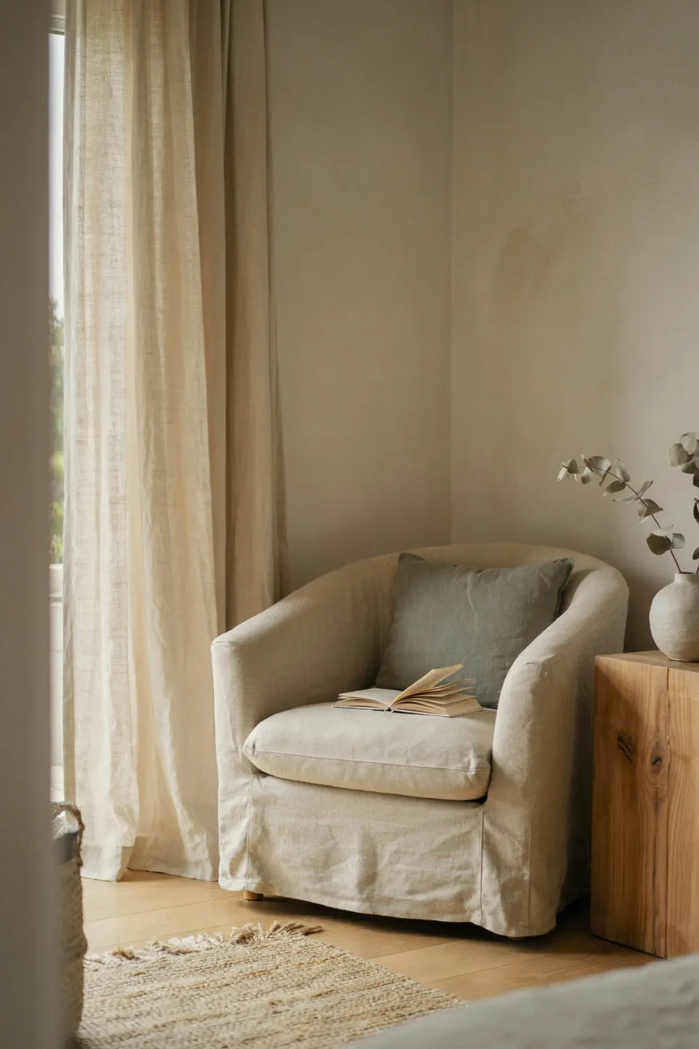 Earthy bedroom corner with a linen armchair, sage green cushion, and natural wood nightstand