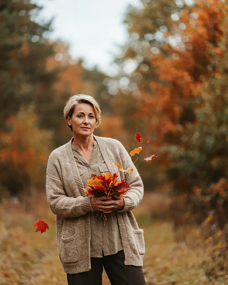 Samantha Jones, founder of The Hazel Cottage, walking through an autumn forest holding fallen maple leaves