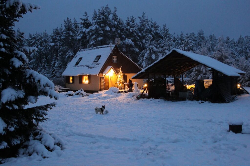 Cozy cottage in winter snow at dusk with warm glowing windows